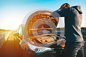 Stressed man with his broken car on the highway roadside at sunset