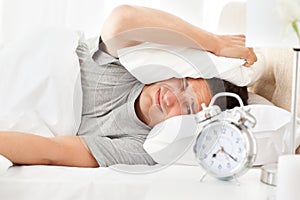 Stressed man looking at his alarm clock ringing