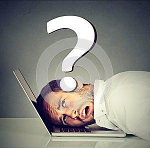 Stressed man resting head on laptop under pressure of problems has questions