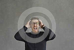 Stressed man touching head and screaming standing over grey studio background