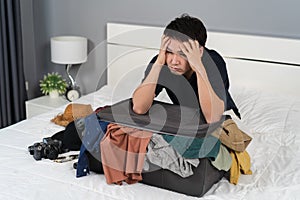 Stressed man trying to close overfilled suitcase on bed