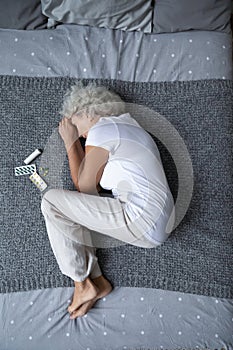 Stressed mature retired woman lying on bed in fetal position.