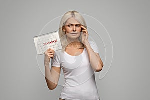 Stressed Mature Woman Looking At Her Menstrual Calendar With Crossed Out Dates photo