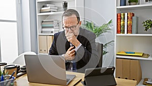 Stressed middle-aged man with grey hair, working hard in business, coughing at his office desk despite illness