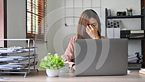Stressed millennial Asian businesswoman suffering from headache or eyes strain