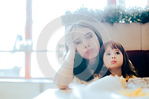 Stressed Mom Sitting with her Child in a Restaurant Booth