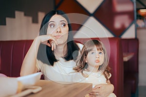 Stressed Mom Sitting with her Child in a Restaurant Booth