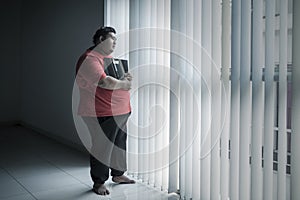 Stressed obese man holds a scale near the window