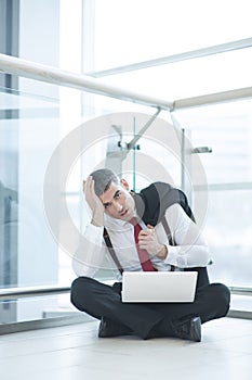 Stressed out businessman seated on floor working at laptop