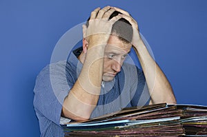 Stressed out man at work in front of a pile of files.