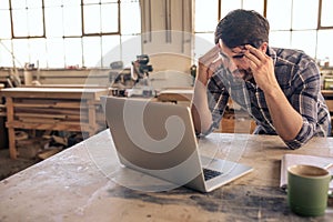 Stressed out woodworker using a laptop in his carpentry studio