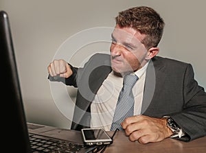 Stressed and overwhelmed businessman in suit and tie working at office laptop computer desk screaming desperate and upset in