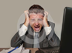 Stressed and overwhelmed businessman in suit and tie working at office laptop computer desk screaming desperate and upset in