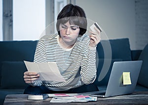 Stressed and overwhelmed young woman paying credit card debts and bills on laptop