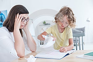 Stressed psychotherapist having a headache during a meeting with a rebellious child with behavioral disorders. The kid is tearing