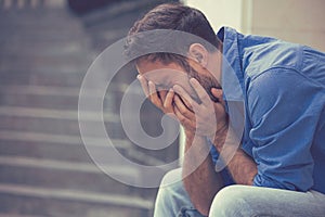 Stressed sad crying man sitting outside holding head with hands photo