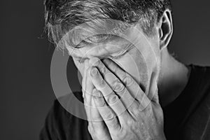 Stressed and sad man covering his face with hands. Sadness, despair, tragedy concept. Monochrome