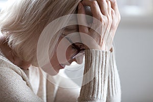 Sad tired senior woman holding head in hands feeling headache photo