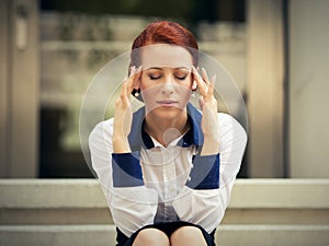 Stressed sad woman sitting outdoors having headache. City urban life style stress