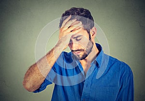 Stressed sad young man looking down on gray wall background