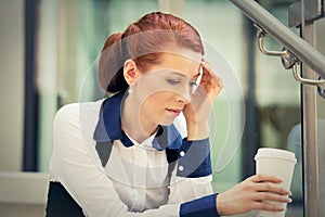 Stressed sad young woman with coffee cup sitting outdoors. City urban life style stress