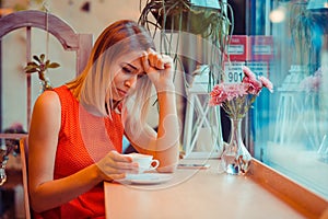Stressed sad young woman with coffee cup sitting in a trendy cafe