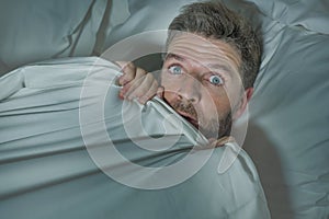 Stressed and scared man alone in bed awake at night in fear after having a nightmare feeling paranoid holding the blanket in