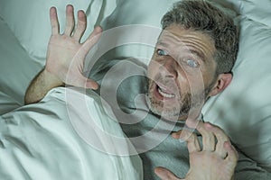 Stressed and scared man alone in bed awake at night in fear after having a nightmare feeling paranoid holding the blanket in