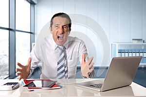 Stressed senior businessman with tie in crisis working on computer laptop at desk in stress under pressure