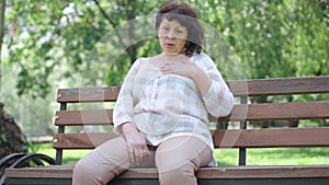 Stressed senior Caucasian woman having symptoms of heart attack in sunny summer park. Portrait of old ill retiree
