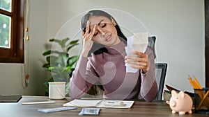 A stressed and serious Asian woman sitting at a table worried about her monthly expenses