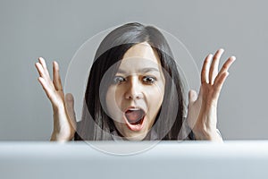 Stressed shocked business woman sitting at table in front of laptop looking stunned wide open mouth