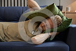 Stressed soldier man covering ears with pillow trying drown out voices in head