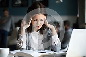 Stressed student having headache preparing for test exam in cafe