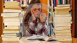 Stressed student studying and taking notes in the library surrounded by books