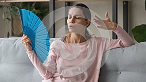 Stressed sweaty woman waving fan suffer from heat at home