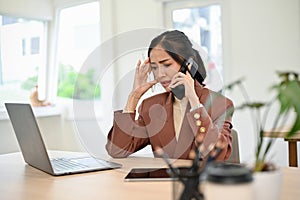 Stressed and thoughtful Asian businesswoman talking on then phone at her desk