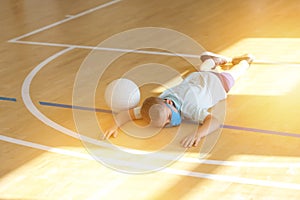 Stressed tired exhausted child with blue mask and  ball in a physical education lesson. Safe back to school during pandemic concep