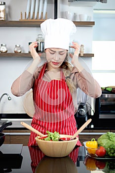 Stressed unhappy Asian beautiful woman with apron chef hat putting head in hands at kitchen. Young female chef thinks so hard