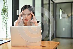 Stressed and upset Asian female office worker looking at her laptop screen, pensive