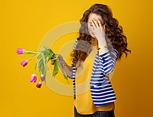 Stressed woman against yellow background with wilted flowers