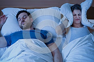 Stressed woman covering ears with a pillow as she is annoyed by the snoring of her boyfriend