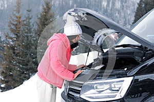 Stressed woman near broken car on winter day