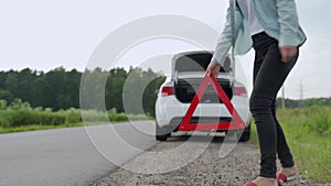 Stressed woman putting emergency sign on the road. Woman having problems with car, stopped her vehicle on the roadside
