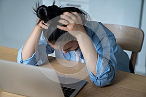 Stressed woman sitting at desk with laptop holding head in hands having online business problems