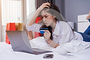 stressed woman using laptop for online shopping on bed, and having problem with blocked credit card