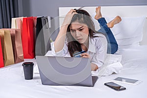 stressed woman using laptop for online shopping on bed, and having problem with blocked credit card