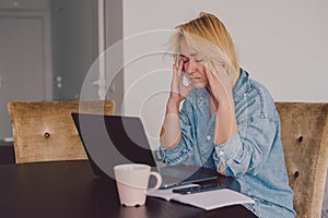 Stressed woman working from home on laptop looking worried, overwhelmed. Exhausted female working remotely during social