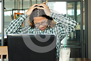 Stressed young Asian business man with hands on head feeling tired against his work in office. Exhausted and overwork job concept.