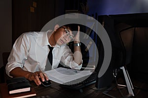 Stressed Young asian business man working late night alone in office late his eyes are gonna closing at table and looking headache